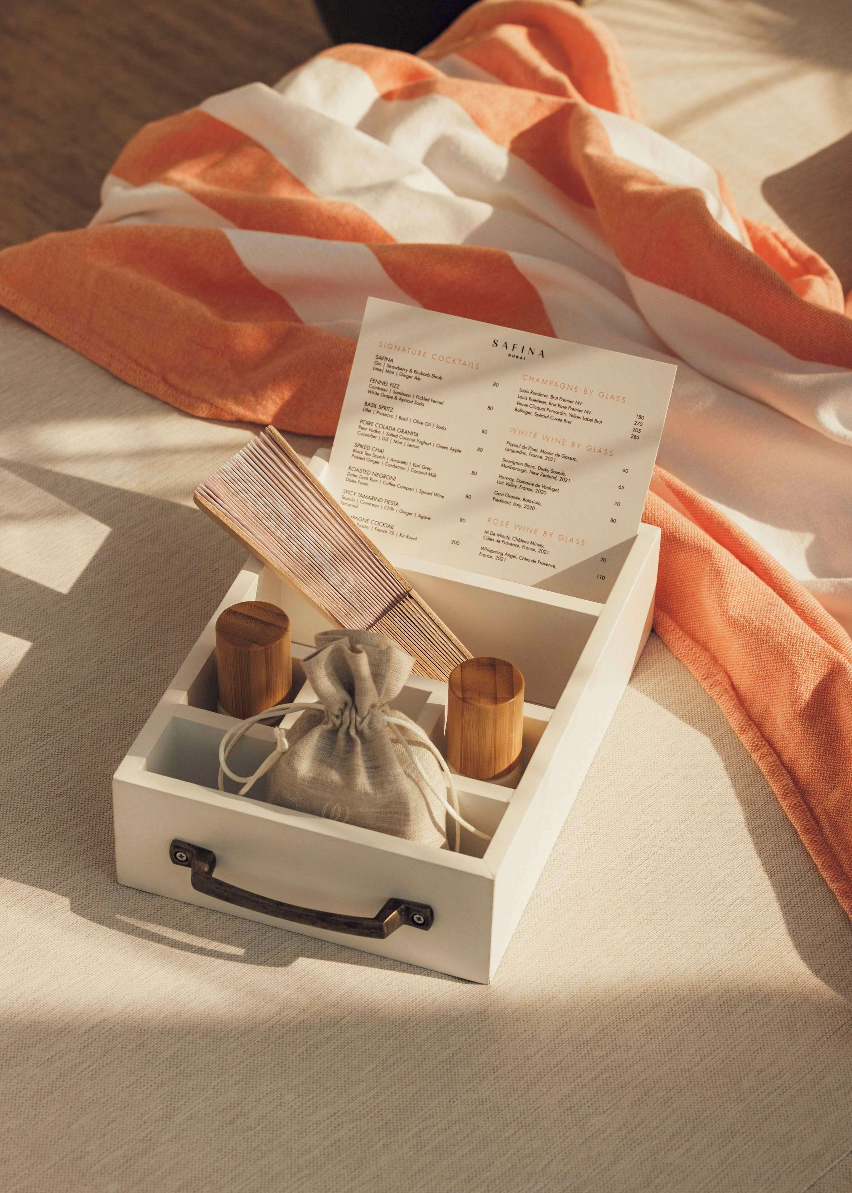 Una caja blanca ordenada con un menú sobre una cama con una manta a rayas naranja y blanca.