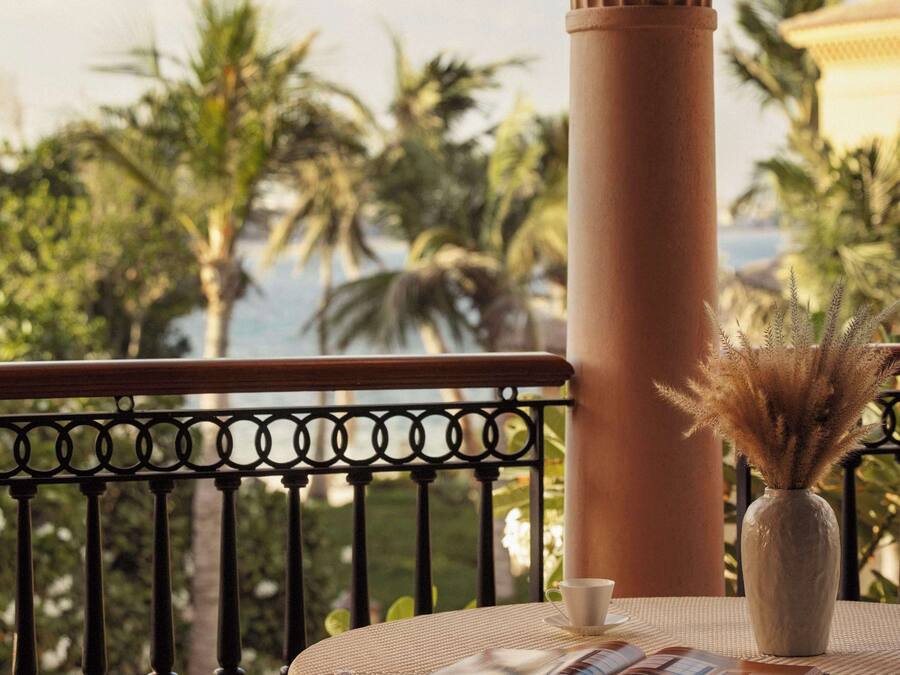 A balcony with a round table, a vase with dried plants, and a cushion.
