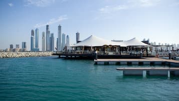 A waterfront area with a row of white tents, a dock, and a city skyline in the background.