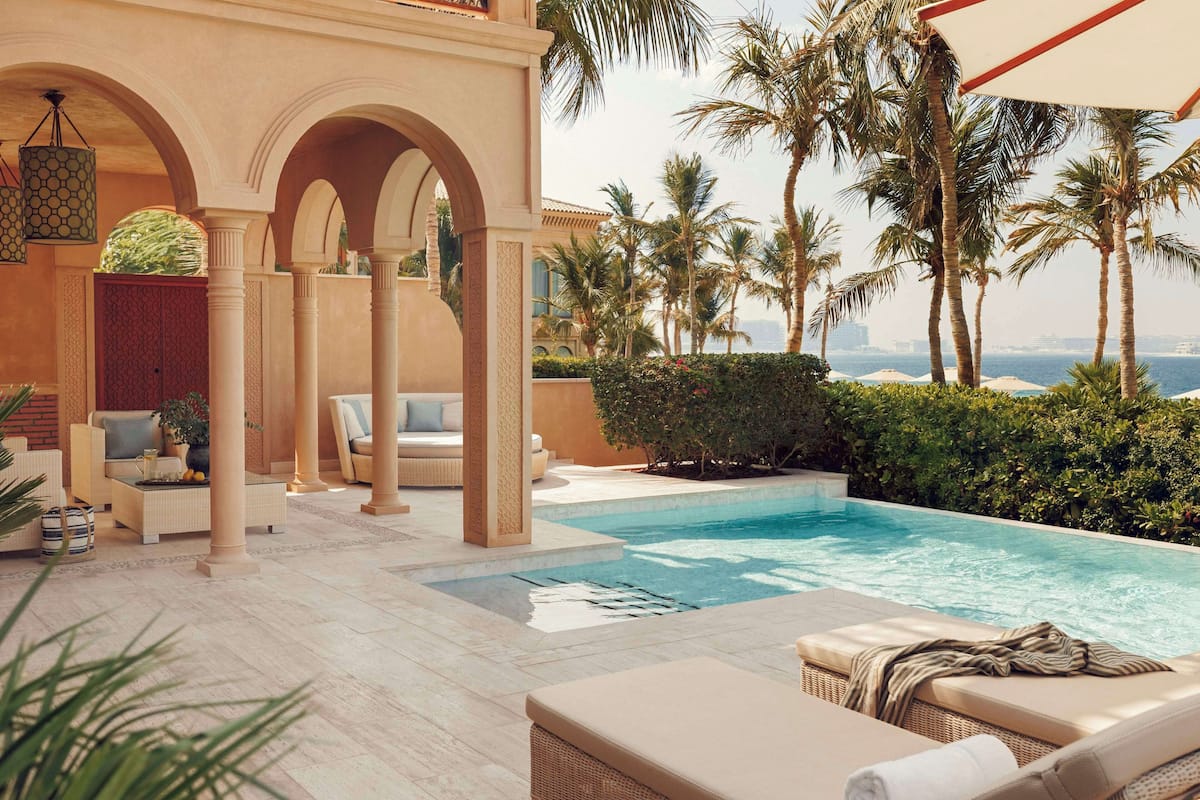 A poolside area with lounge chairs, a seating area with sofas, and a view of the sea.