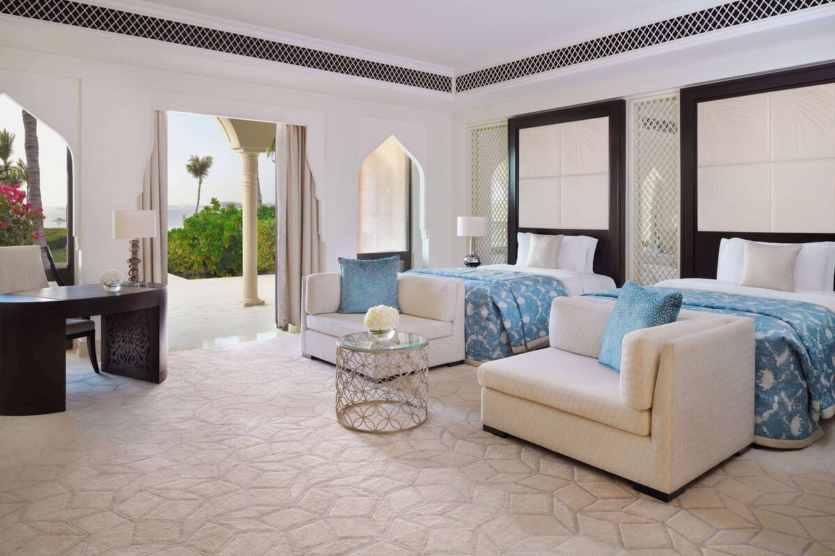 A hotel room with a large bed, two sofas, a small table, and a view of the outdoors.