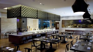 A modern restaurant with a long counter, multiple tables, and a high ceiling with decorative lighting. - IIDL Suites (New Delhi)
