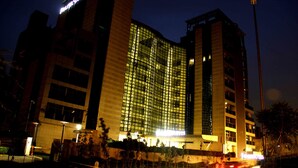 A multi-story hotel with a modern glass facade, illuminated windows, and a prominent sign at the top. - IIDL Suites (New Delhi)