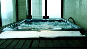 A hot tub with a view of the city through large windows. - IIDL Suites (New Delhi)