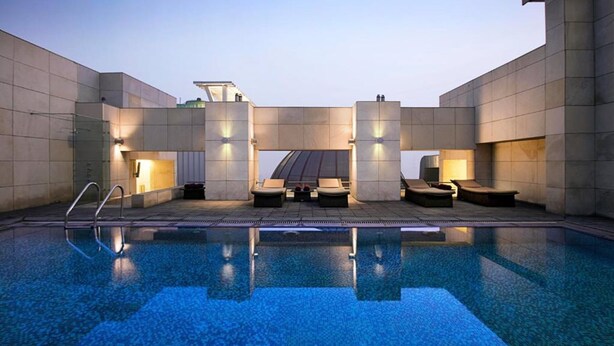 A modern indoor pool area with a clear pool, lounge chairs, and a geometric architectural design. - IIDL Suites (New Delhi)