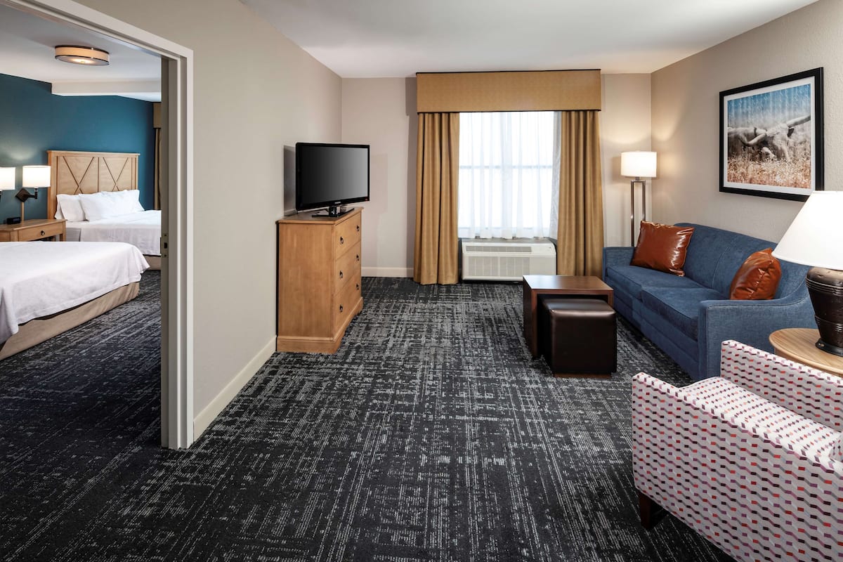 A hotel room with a bed, a sofa, a TV, a desk, and a window with curtains.