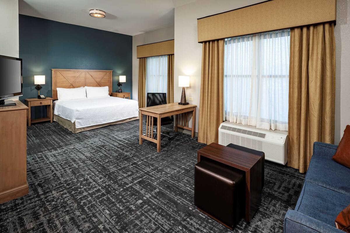 A hotel room with a large bed, a desk, a TV, a sofa, and a window with curtains.