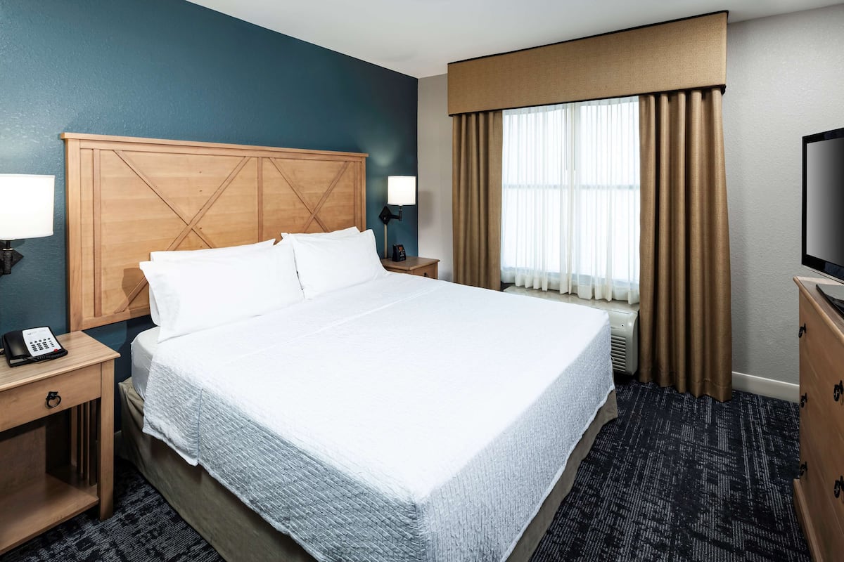 A hotel room with a large bed, bedside tables, a TV, and a window with curtains.