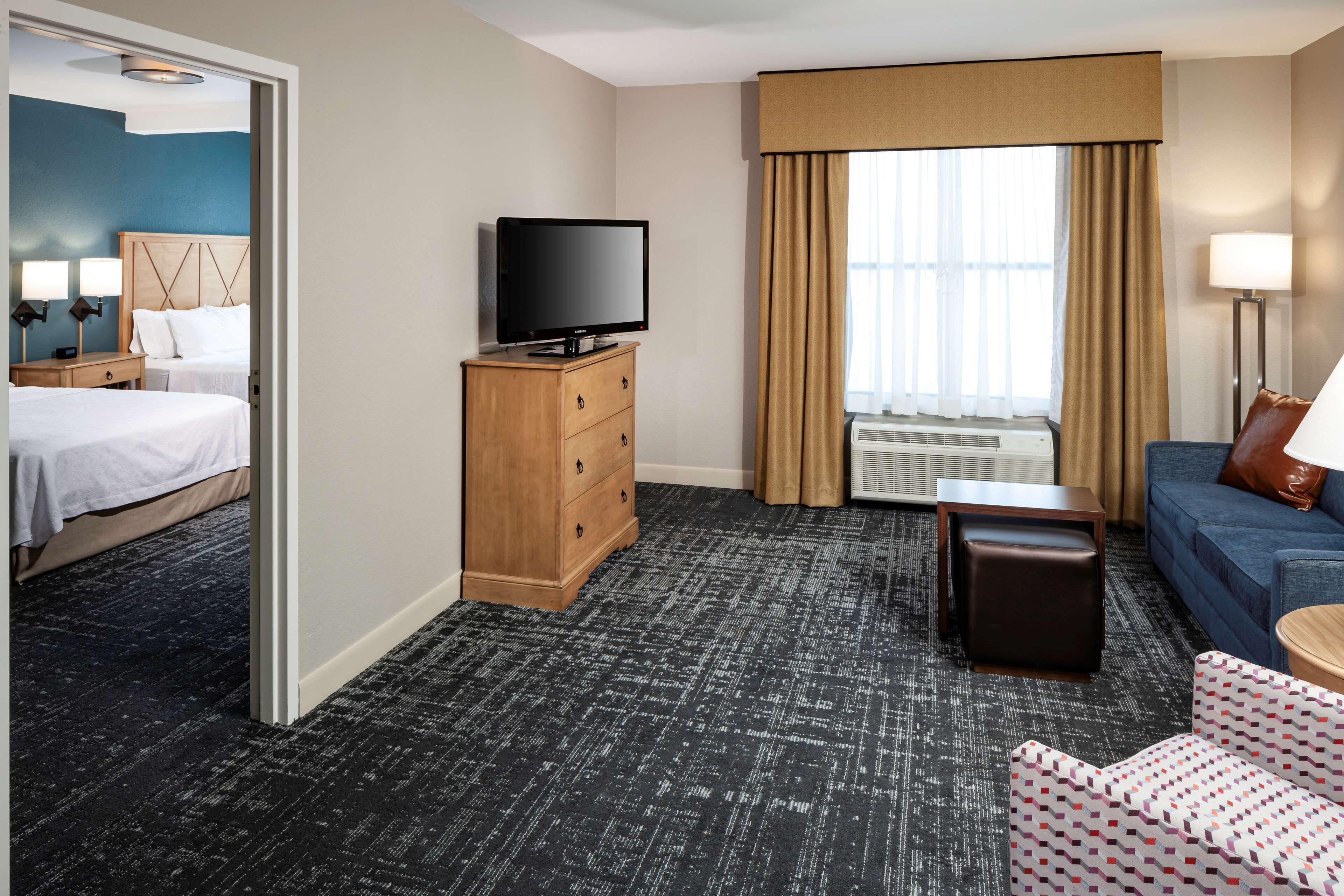 A hotel room with a bed, a TV on a wooden dresser, a sofa, a small table, and a window with curtains.