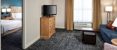 A hotel room with a bed, a TV on a wooden dresser, a sofa, a small table, and a window with curtains.
