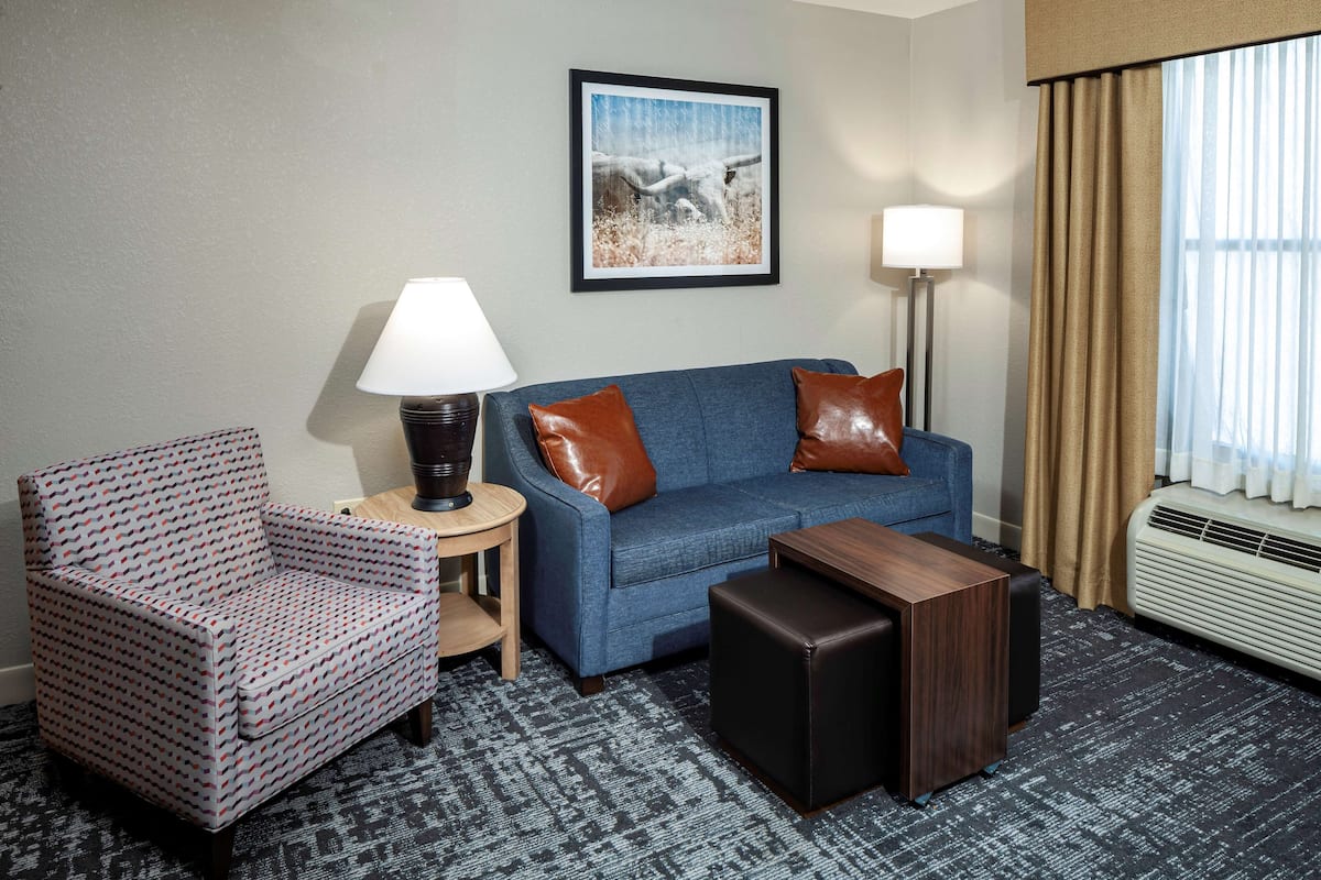 A hotel room with a blue sofa, a patterned armchair, a small table, and a framed picture on the wall.