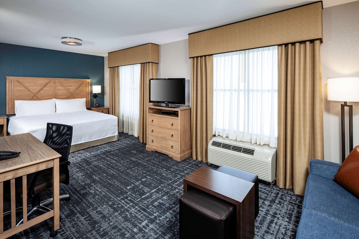 A hotel room with a bed, a desk, a television, a sofa, and a window with curtains.