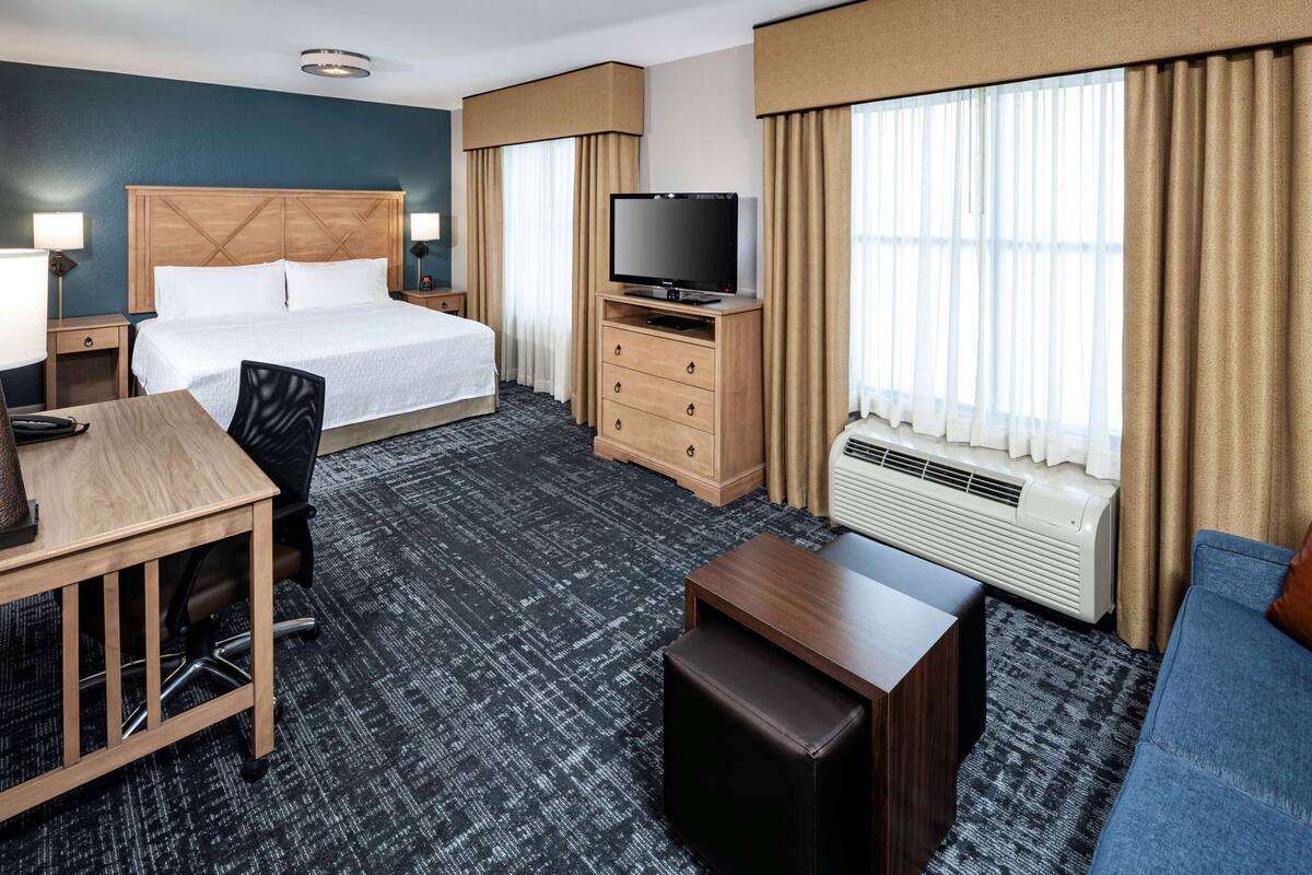 A hotel room with a bed, desk, chair, TV, dresser, and a sofa.
