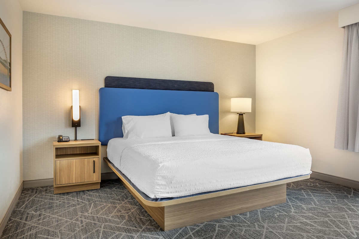 Une chambre d’hôtel avec un lit, une table de chevet, une lampe et un luminaire fixé au mur.