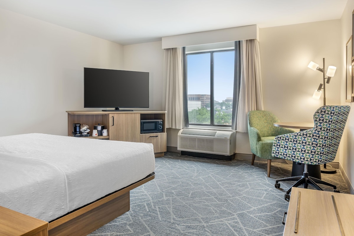 Une chambre d’hôtel équipée d’un lit, d’un bureau avec un t éléviseur à écran plat, d’une chaise, d’une machine à café et d’un climatiseur.