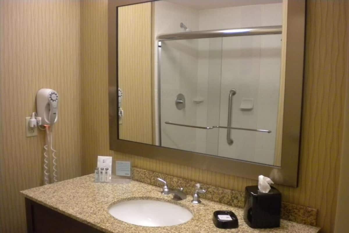 A bathroom with a sink, mirror, shower, and hairdryer.