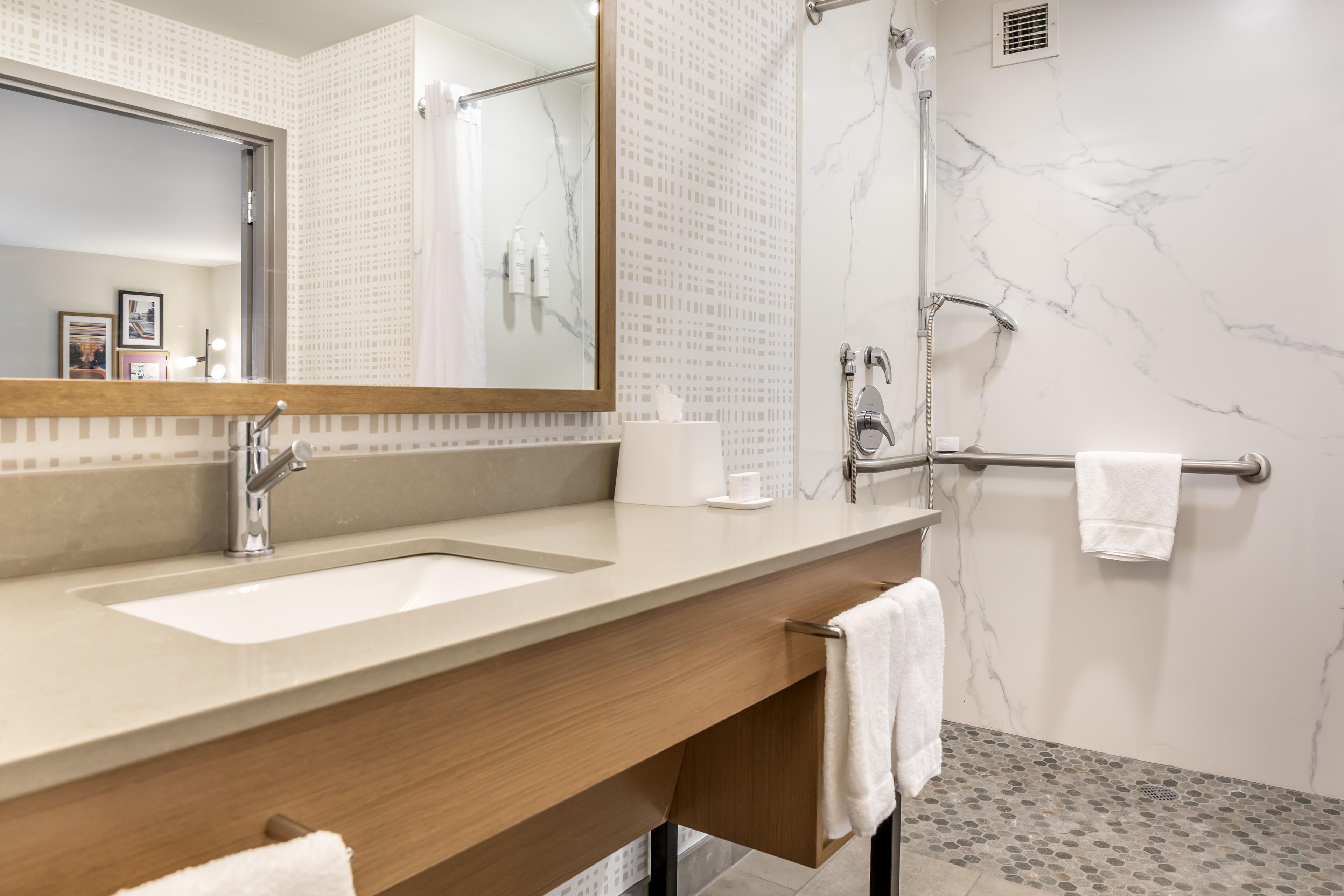 A modern bathroom with a large mirror, two sinks, a shower, and a towel rack.