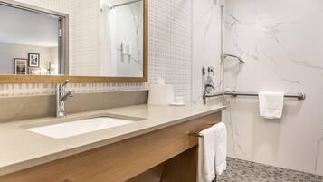 A modern bathroom with a large mirror, two sinks, a shower, and a towel rack.