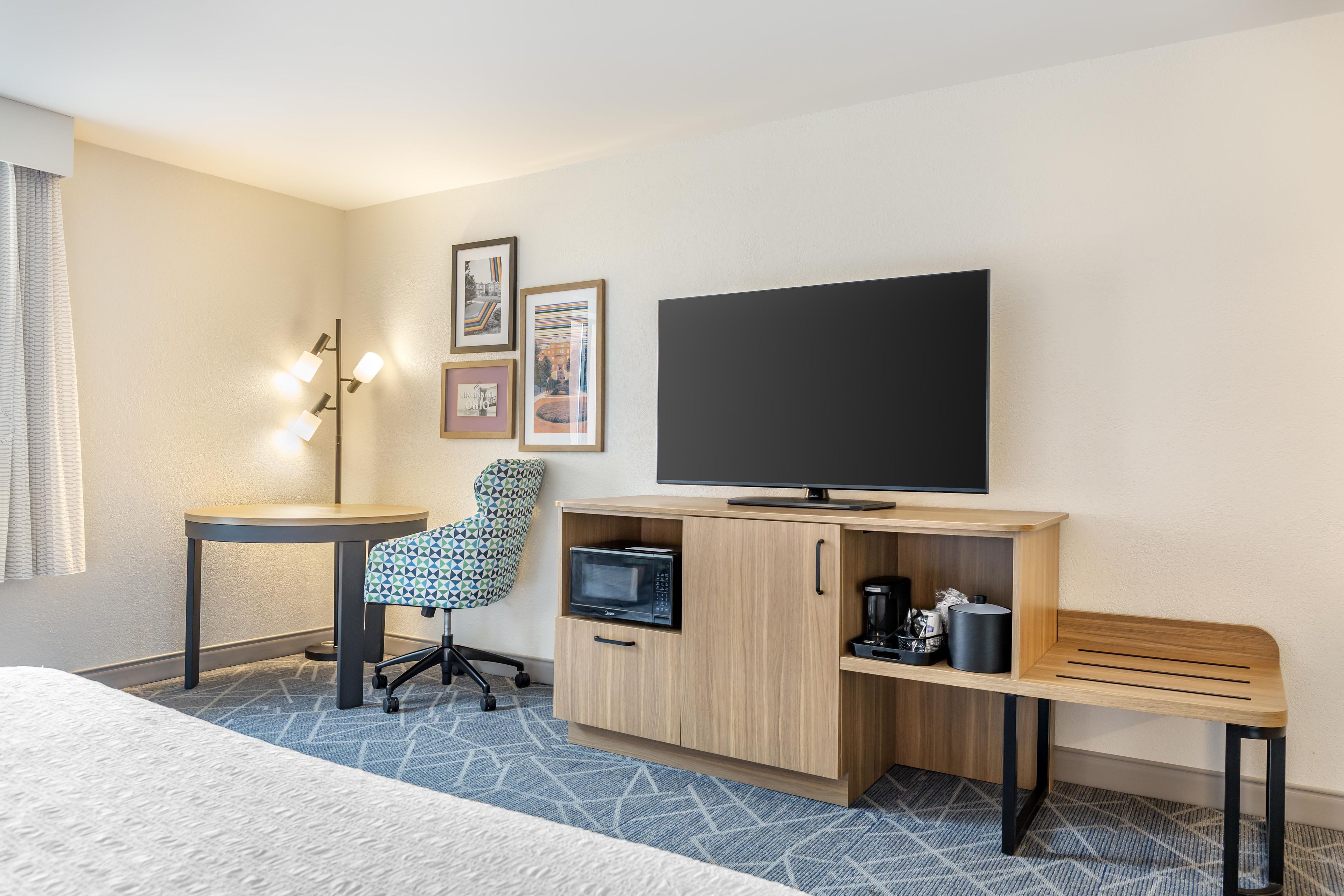 A hotel room with a bed, a desk, a chair, a television, a microwave, and a coffee maker.