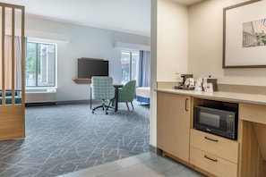 Une chambre d’hôtel moderne dotée d’une kitchenette, d’une grande fenêtre, d’un bureau et d’une chaise.