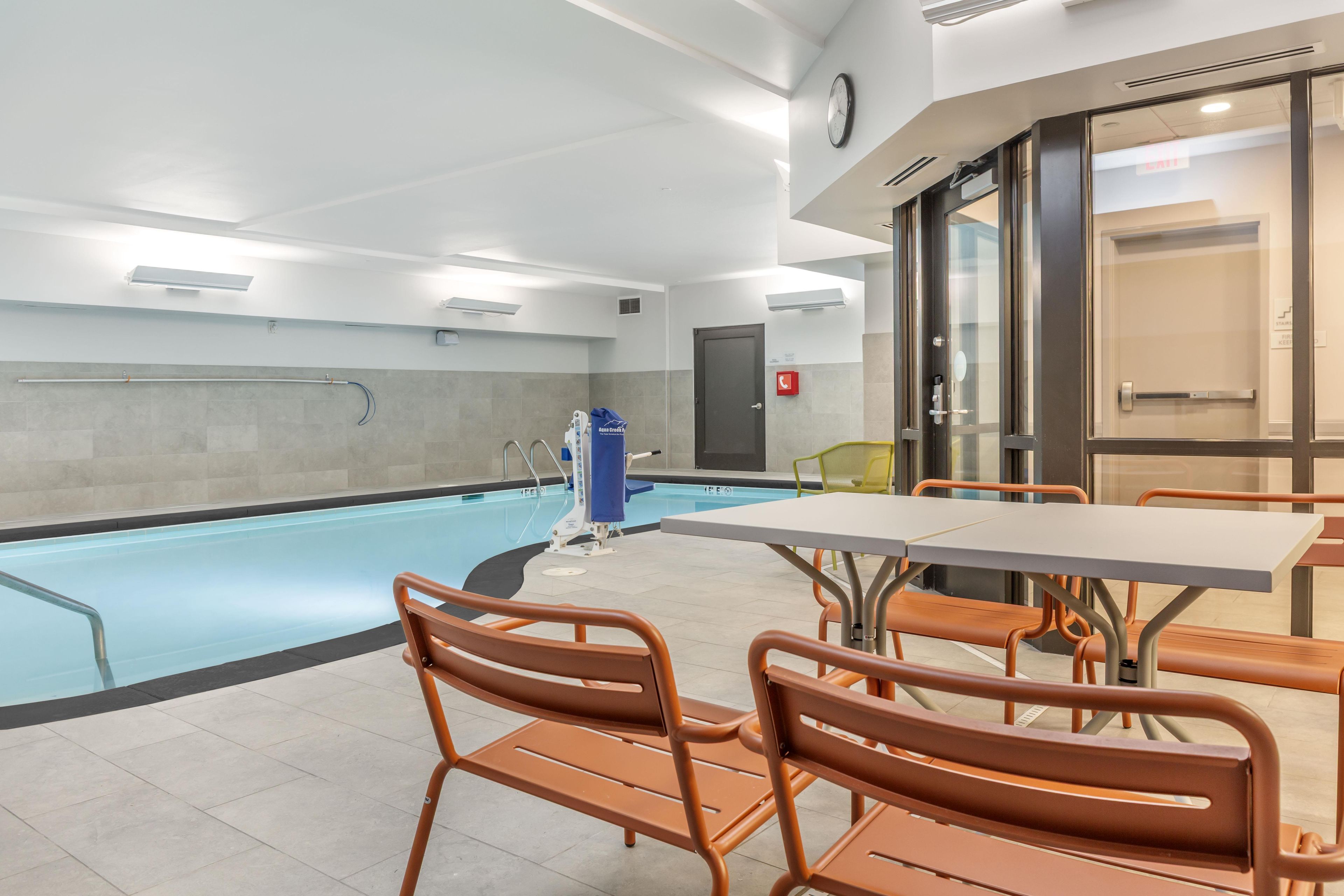 Zona de piscina con silla de salvavidas, escalera para piscina y mesa con sillas.