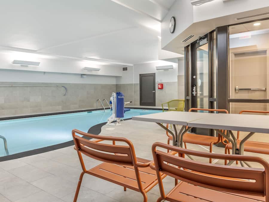 Een zwembadgedeelte met een strandstoel voor de badmeester, een zwemtrap en een tafel met stoelen.