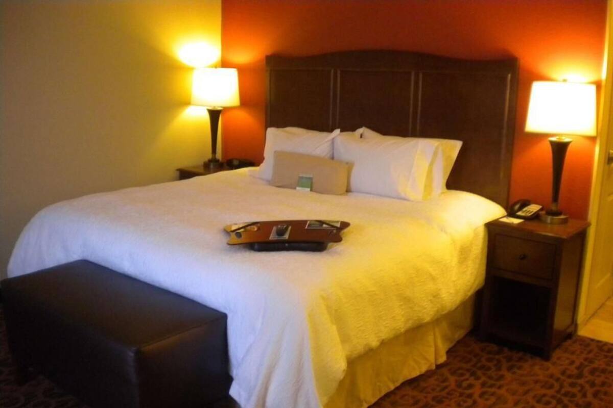 A hotel room with a bed, two bedside tables, a nightstand, a bench, and two lamps.