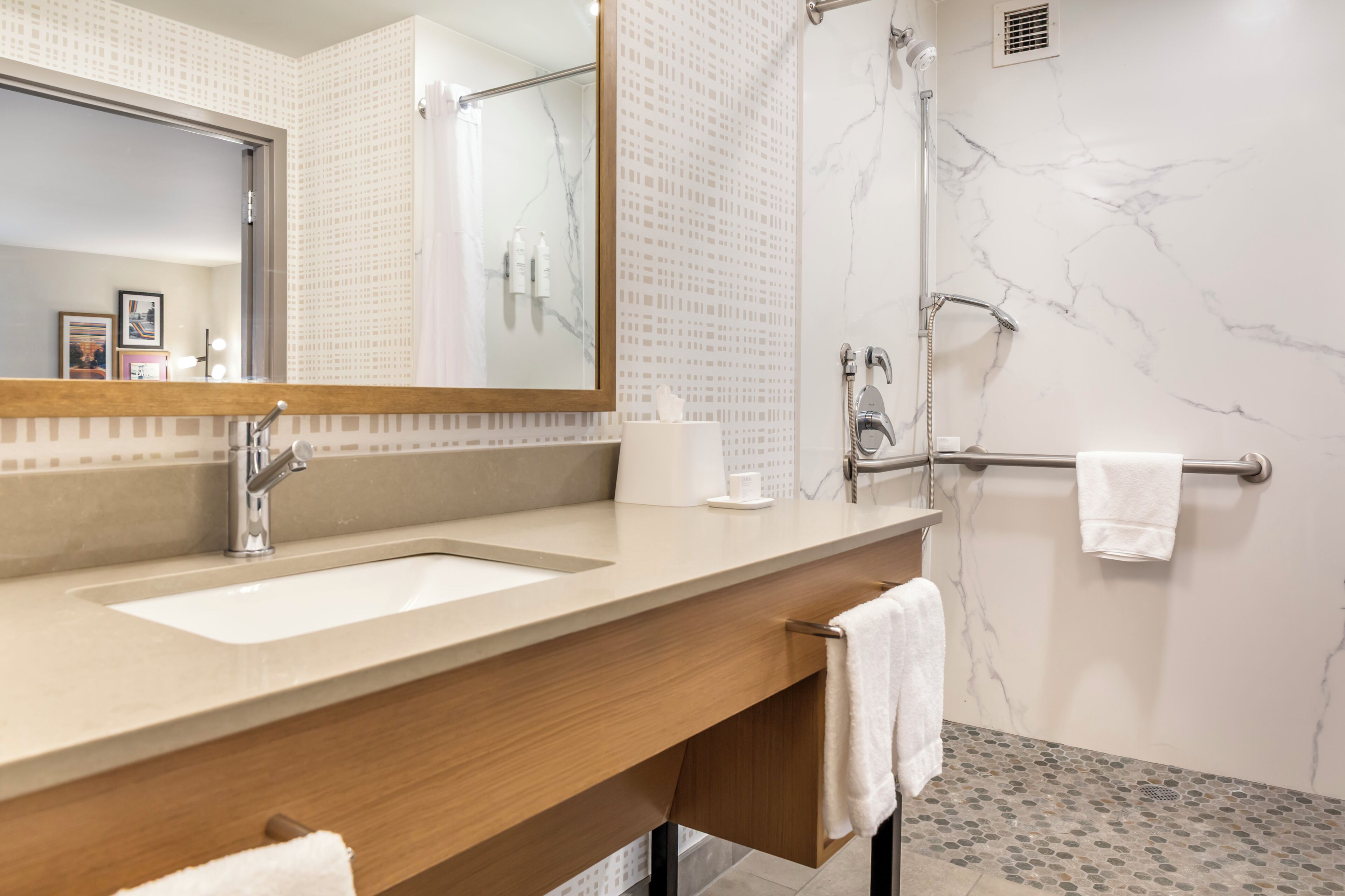 A modern bathroom with a marble shower, a large mirror, and a wooden vanity.