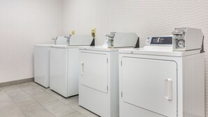 A laundry facility with four white front-loading washers and dryers, a patterned wall, and a tiled floor. - Hampton Inn & Suites Cincinnati/Uptown-University Area (Cincinnati)