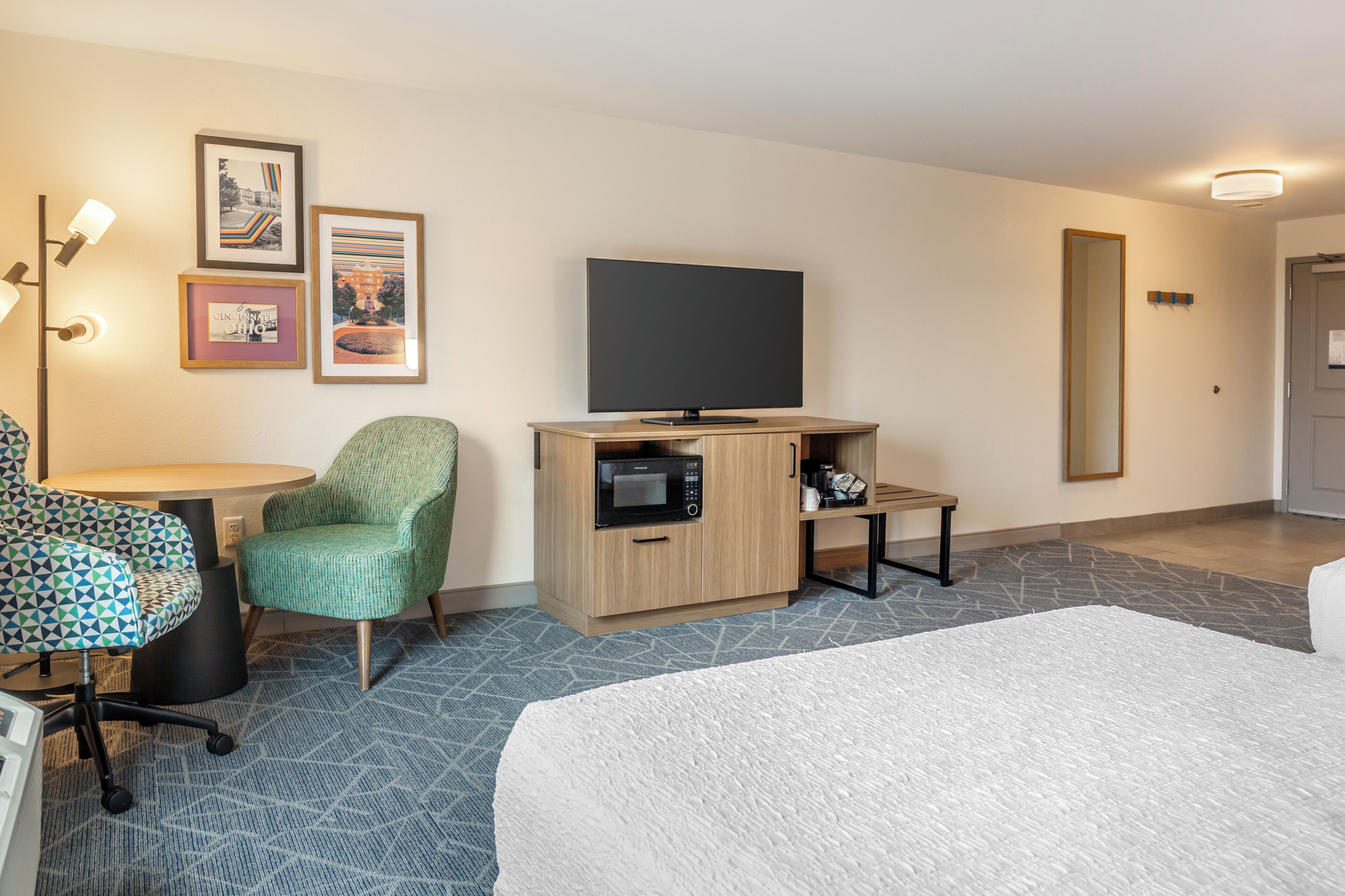 A hotel room with a bed, a desk with a chair, a flat-screen TV, a microwave, and a coffee maker.