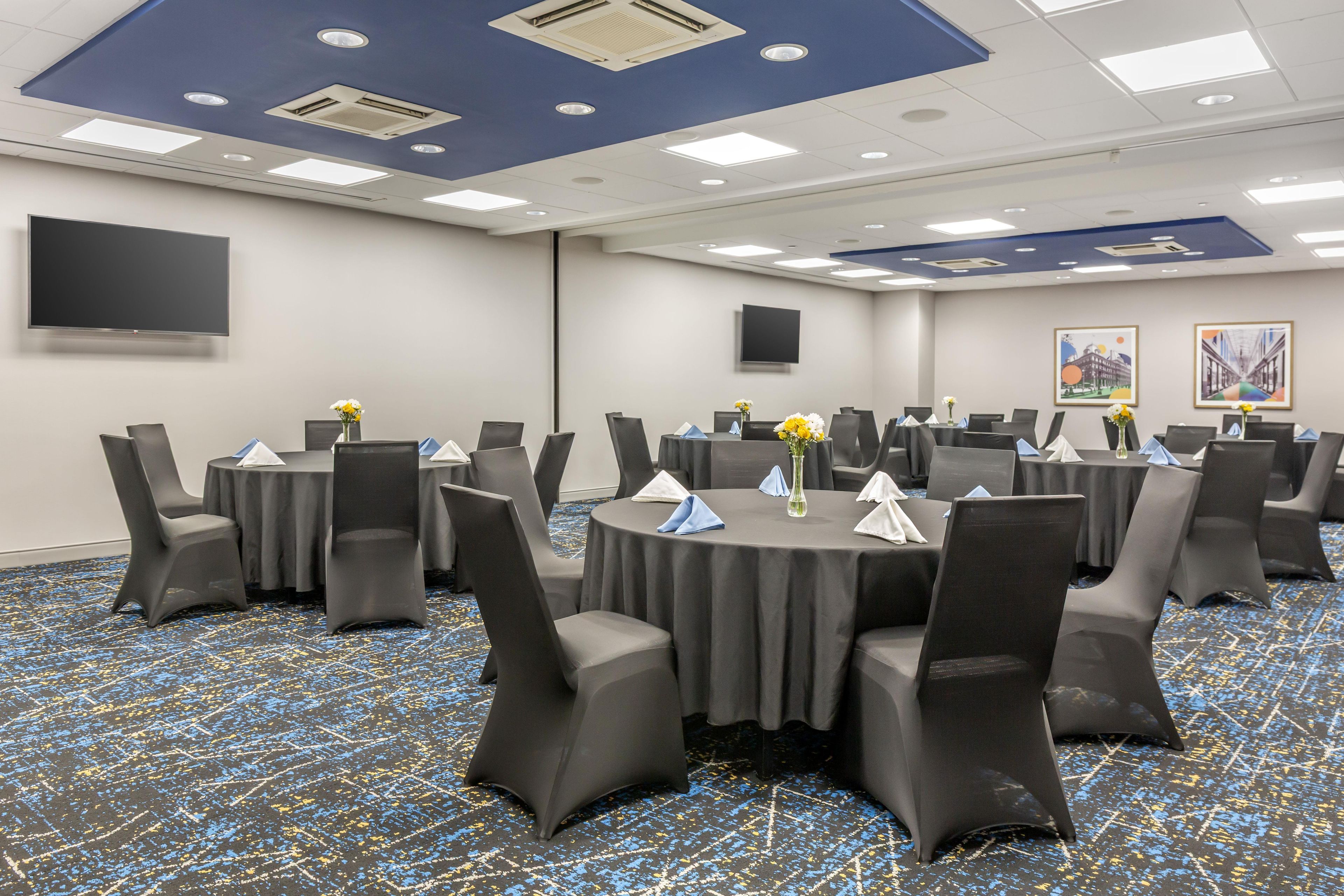 Un salón de conferencias con mesas redondas, sillas y un televisor de pantalla plana en la pared.