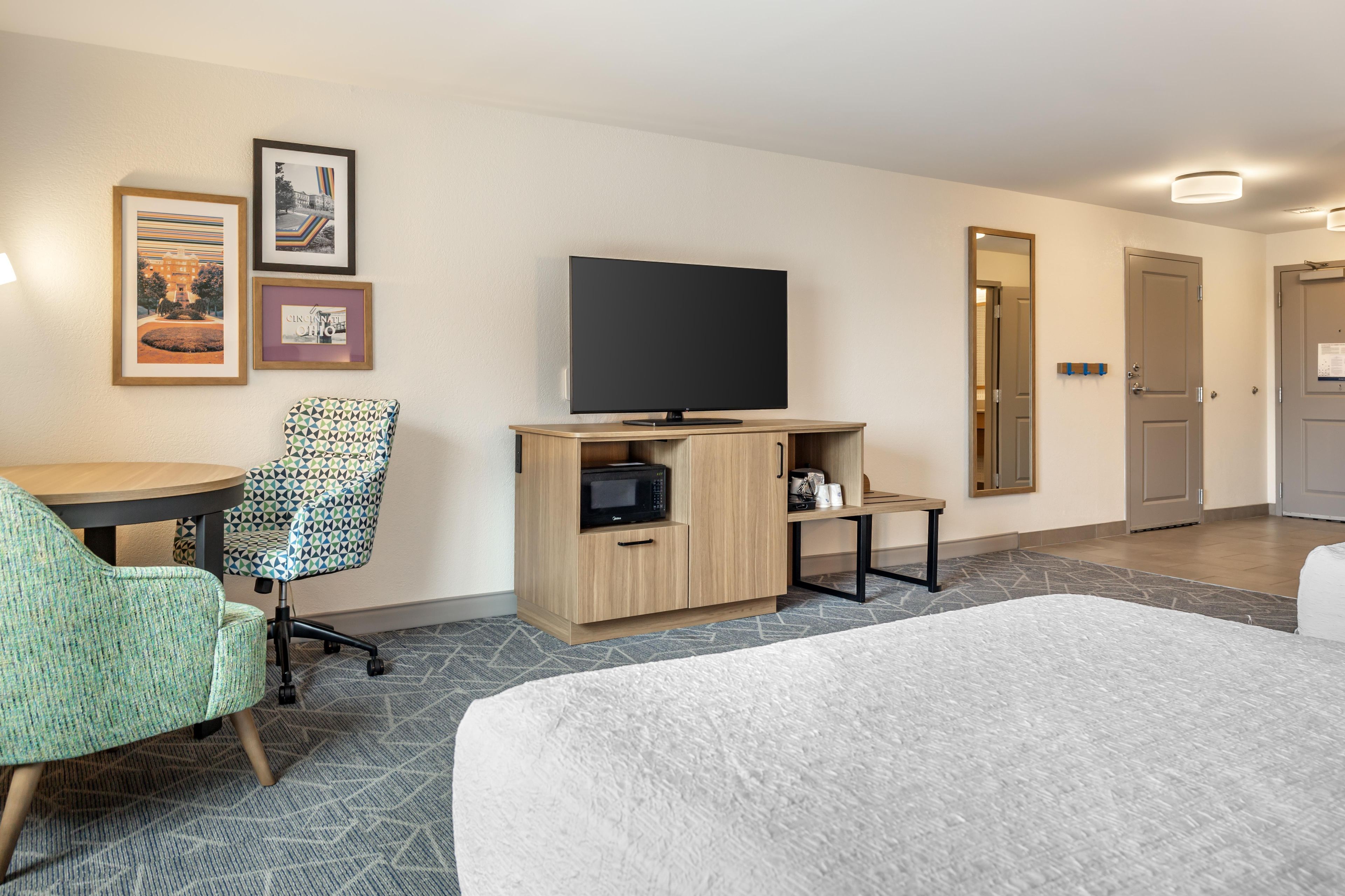 A hotel room with a bed, a desk with a chair, a television, a microwave, and a small cabinet.