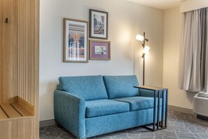 A room with a blue sofa, a small table, a floor lamp, and two framed pictures on the wall. - Hampton Inn & Suites Cincinnati/Uptown-University Area (Cincinnati)