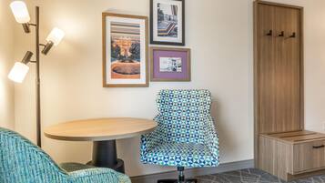 A hotel room with a round table, a patterned armchair, a floor lamp, and a wardrobe.