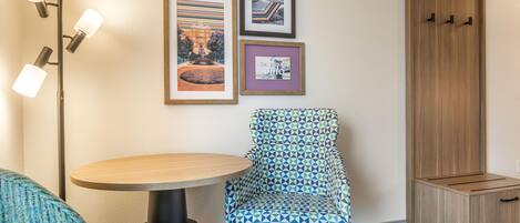 A hotel room with a round table, a patterned armchair, a floor lamp, and a wardrobe.