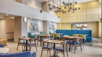 A modern dining area with tables and chairs, a blue sofa, and a hanging light fixture.
