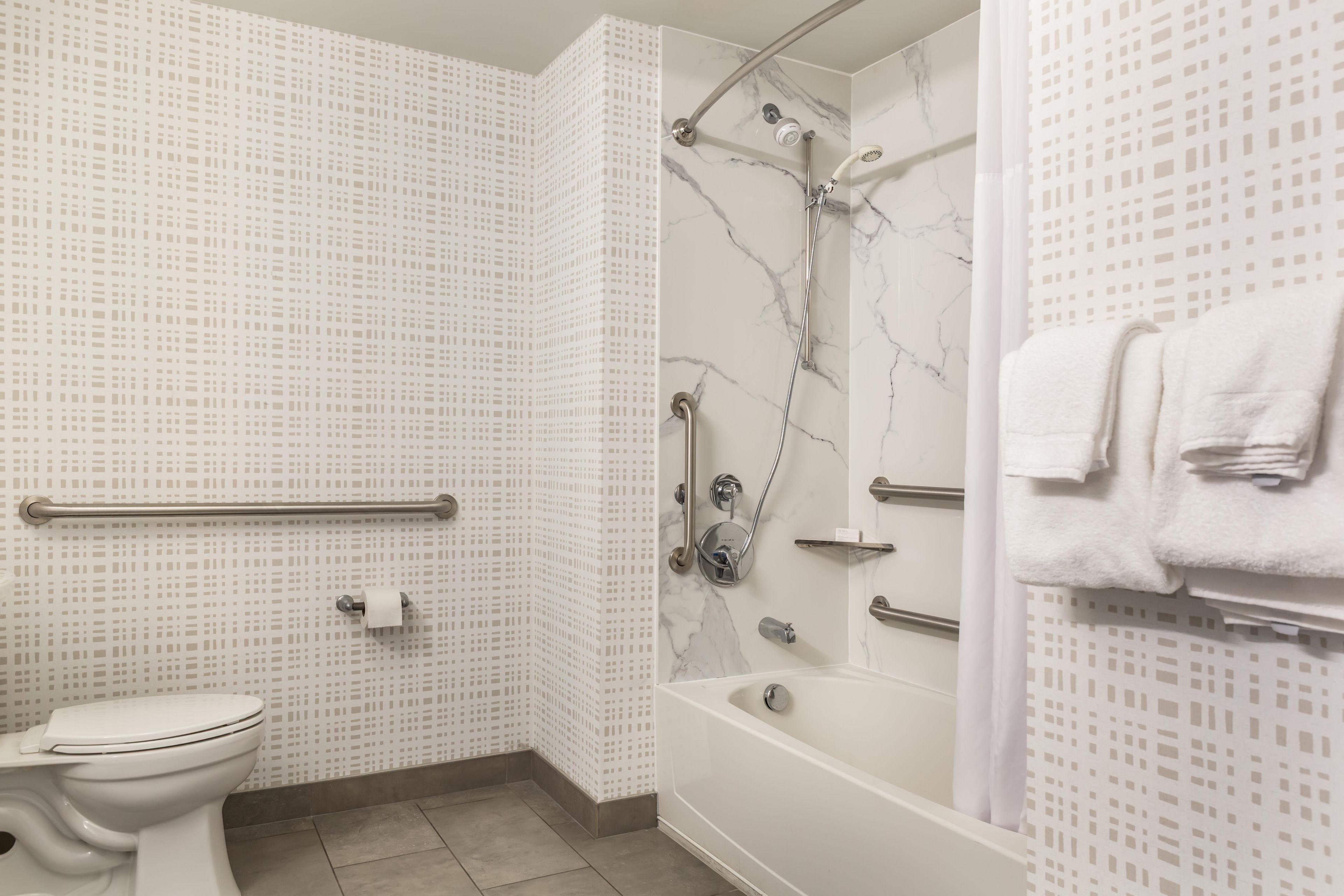 A bathroom with a toilet, a shower with a handheld showerhead, and a bathtub.
