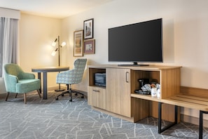A hotel room with a TV, a desk, two chairs, a cabinet with a coffee maker, and a patterned rug. - Hampton Inn & Suites Cincinnati/Uptown-University Area (Cincinnati)