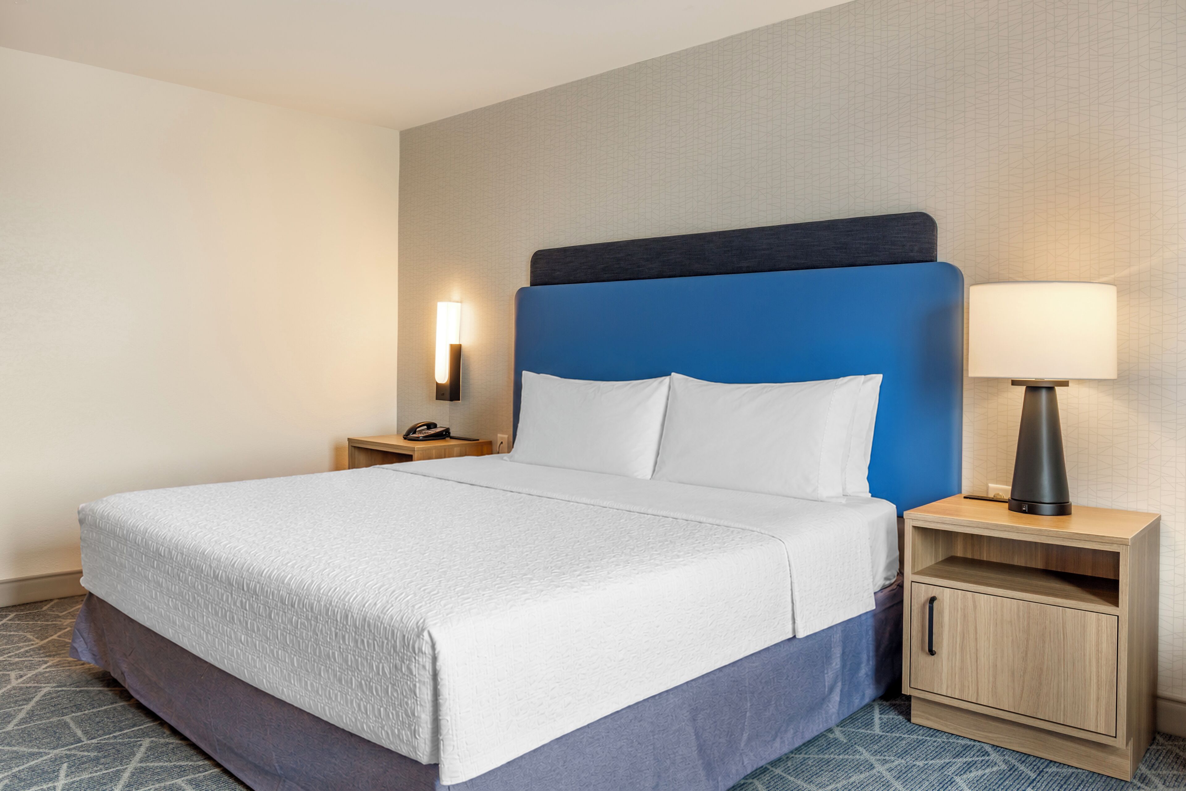 A hotel room with a bed, bedside tables, a lamp, and a cabinet.