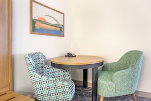 Une pièce avec une table ronde, deux chaises à motifs, un tableau encadré au mur et un plancher en bois.