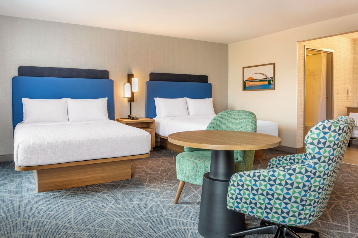 Une chambre d’hôtel avec deux lits, une petite table ronde, une chaise et un tableau au mur.