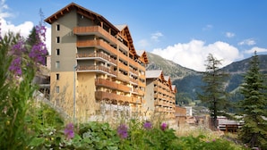 Un hôtel à plusieurs étages, doté de balcons et entouré de montagnes et de verdure.