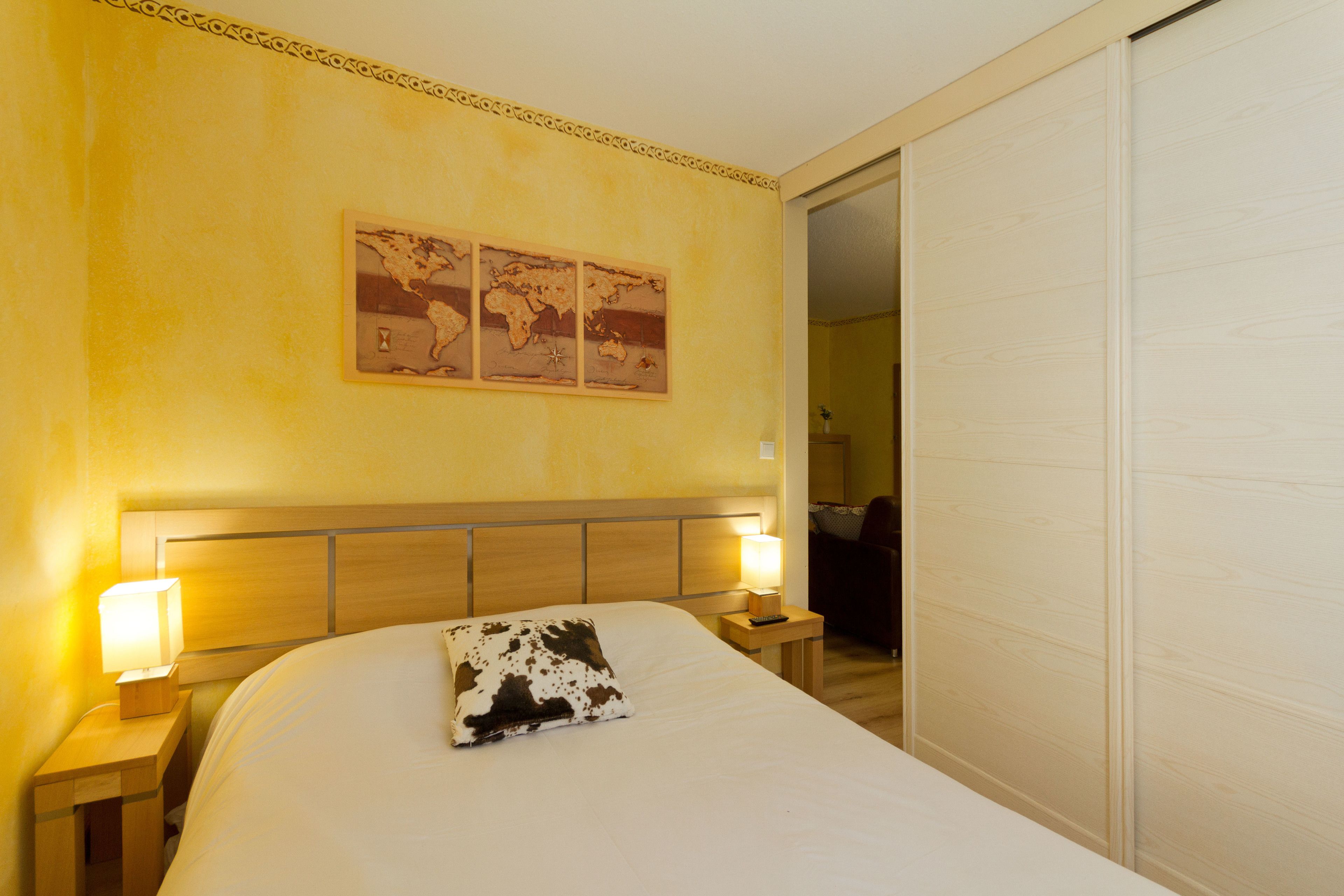 A hotel room with a large bed, two bedside lamps, a wooden headboard, and a world map artwork on the wall.
