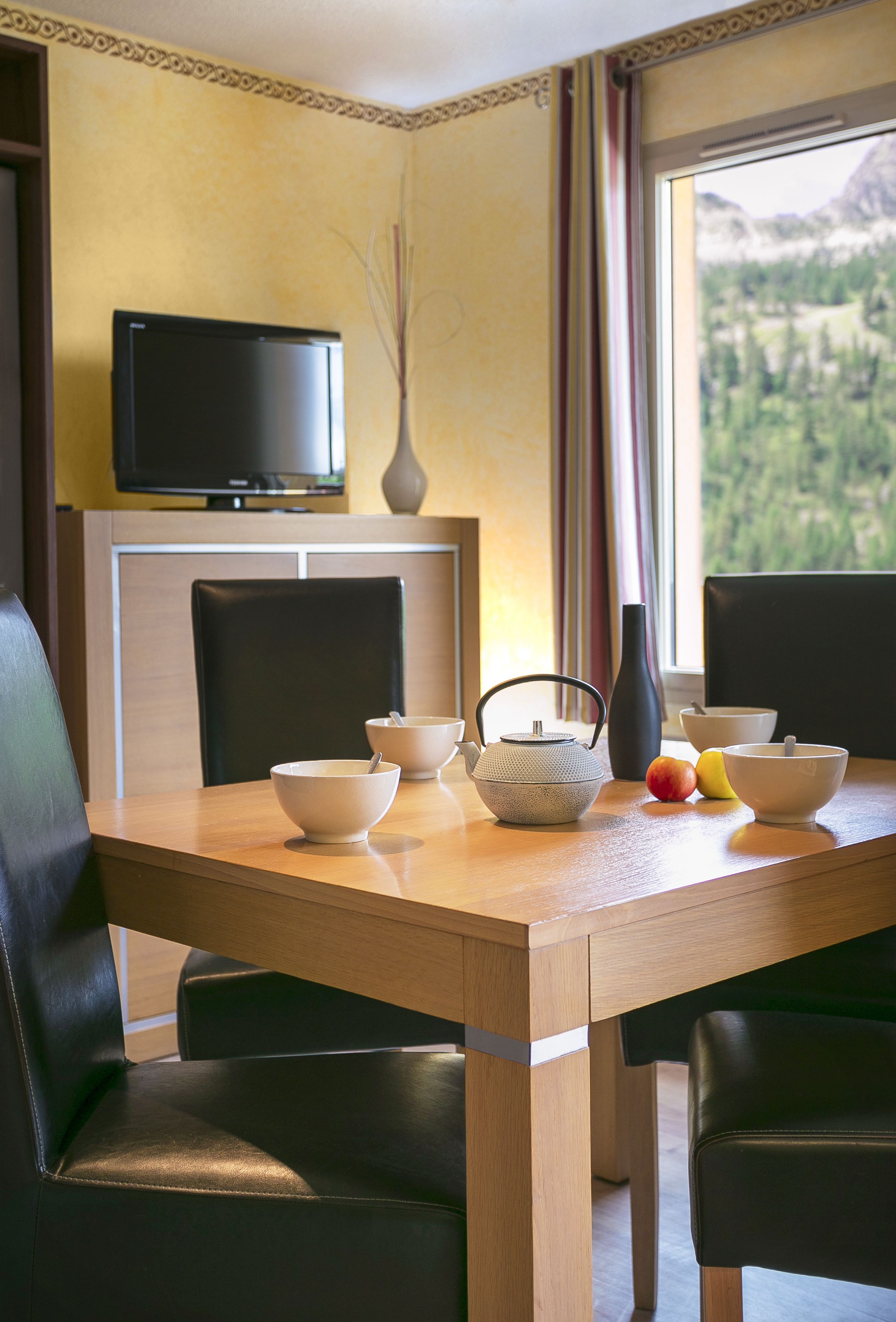 A dining table with chairs, a television above, and a window with a mountain view.