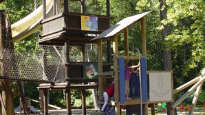 A wooden play structure with multiple levels and slides, surrounded by trees. - Hotel Sportcenter Fünf Dörfer (Trimmis)