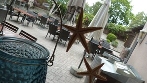 An outdoor patio area with tables and chairs, starfish decorations, and a large blue container. - Hotel Sportcenter Fünf Dörfer (Trimmis)