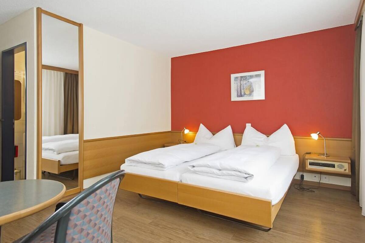 A hotel room with a bed, bedside tables, a chair, and a mirror.