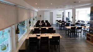 A restaurant with multiple tables and chairs, a long counter with hanging decorations, and a view of the street through large windows. - Hotel Sportcenter Fünf Dörfer (Trimmis)