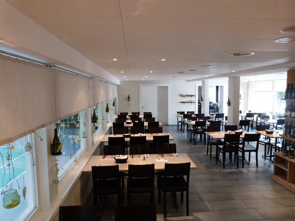 A restaurant with multiple tables and chairs, a long counter with hanging decorations, and a view of the street through large windows.