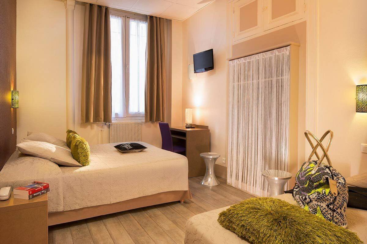 A hotel room with a bed, a desk, a chair, a TV, and a window with curtains.